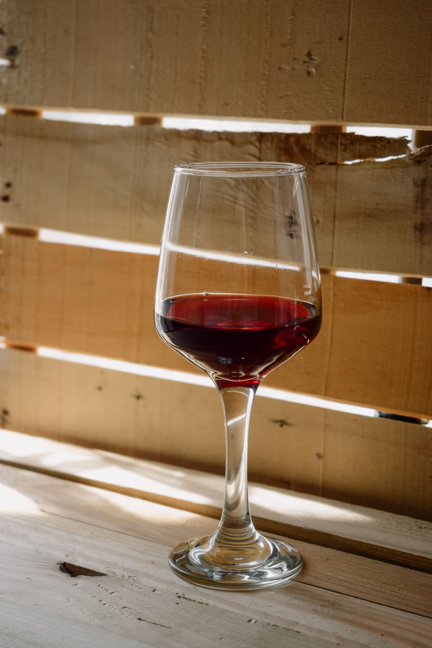 Copa de vino tinto servida a la temperatura adecuada, sobre mesa de madera, bodega de Mendoza