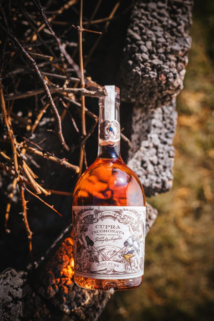 Botella Cupra Incoronata Rosé con luz dramática entre ramas oscuras